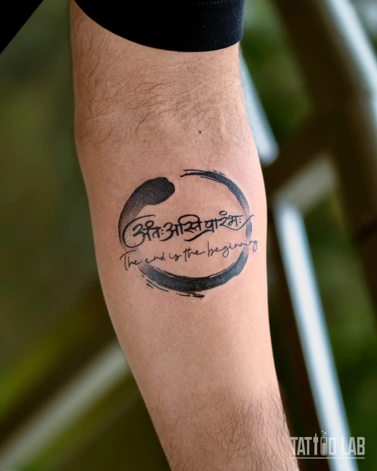 Enso brushstroke circle tattoo on the forearm with Sanskrit script and The end is the beginning lettering, Tattoo Lab, Halifax