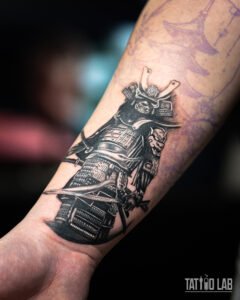 Black and grey realism samurai tattoo in full armour holding a katana on the forearm