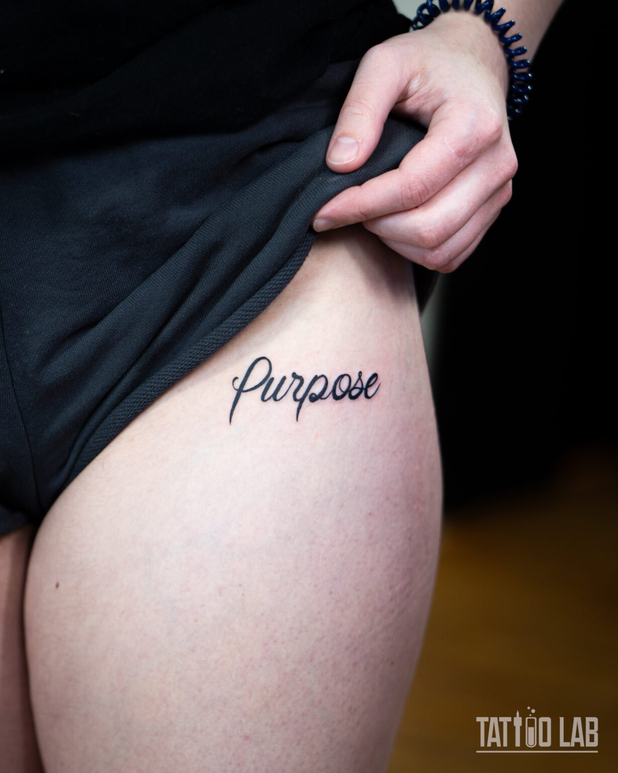 Cursive Purpose script tattoo on the upper thigh in bold black ink, Tattoo Lab, Halifax