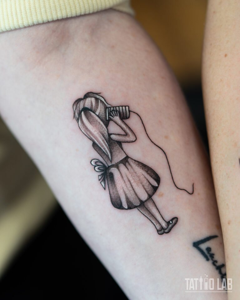 Black and grey tattoo of a girl talking into a tin can phone on the forearm, one half of a matching pair