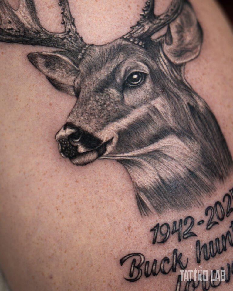 Close-up of a black and grey realistic deer head memorial tattoo with script lettering beneath