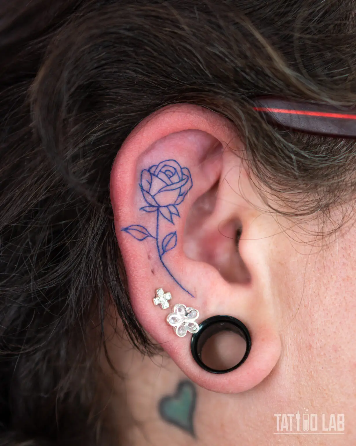 Blue ink fine line rose tattoo on the ear, a delicate outline design with leaves and stem, Tattoo Lab, Halifax