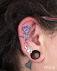 Blue ink fine line rose tattoo on the ear, a delicate outline design with leaves and stem