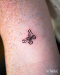 Small fine line butterfly tattoo with soft shading on the wings, a delicate minimalist design