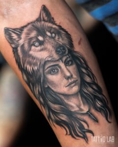 Black and grey realism tattoo of a woman wearing a wolf headdress, with detailed fur and flowing hair
