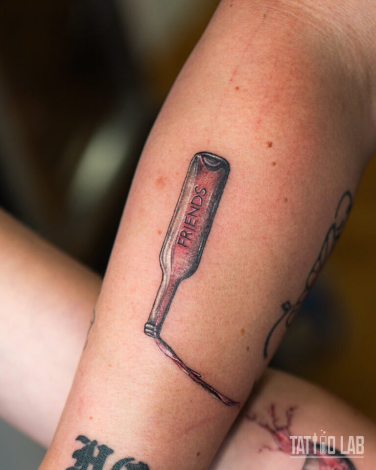 Upside-down wine bottle tattoo labelled "FRIENDS" pouring red wine, half of a matching best friends set