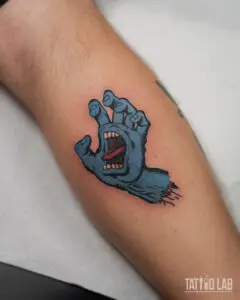 Blue screaming hand tattoo on the calf in bold colour cartoon style with thick black outlines