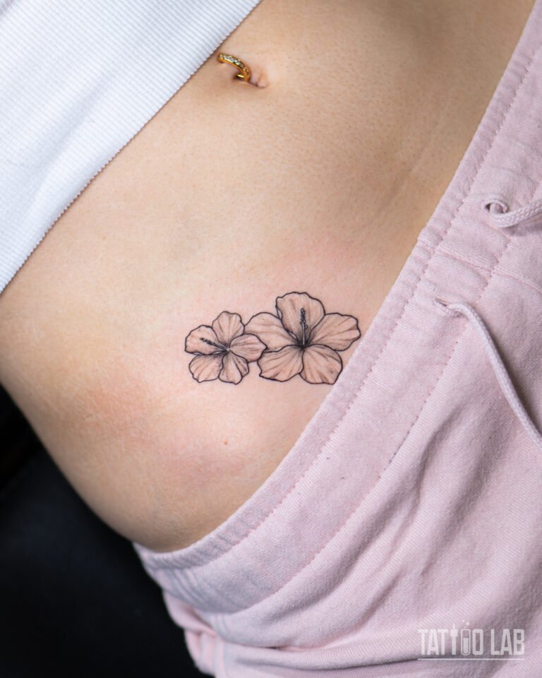 Two hibiscus flowers tattoo on hip in fine line black and grey realism by Tattoo Lab Halifax Nova Scotia.