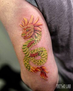 Colour tattoo of an Aztec-style feathered serpent on the back of the arm, with green scales and red and gold feathers