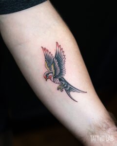 Traditional swallow tattoo on the forearm, old school style with bold black lines and red and yellow accents