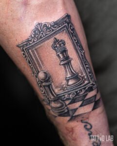 Black and grey realism forearm tattoo of a chess pawn seeing itself as a king in an ornate mirror