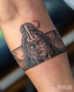 Black and grey realism armband tattoo of Lord Shiva with a crescent moon, trident marking and mountain backdrop