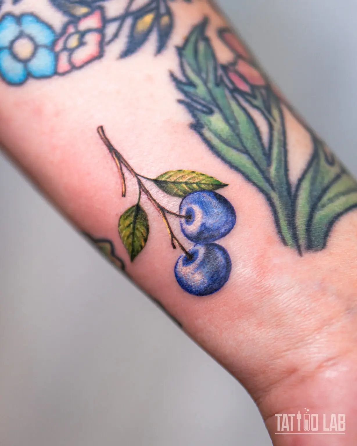 Close-up of one of the matching blueberry sprigs, three berries and leaves in colour realism on the wrist, Tattoo Lab, Halifax