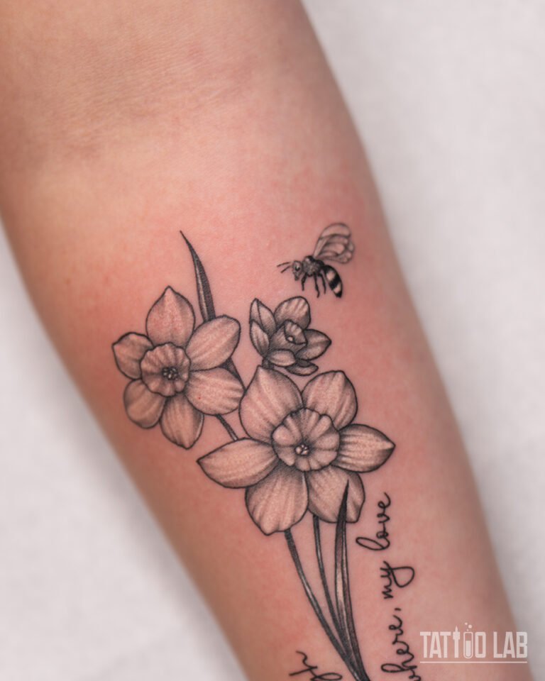 Close-up of a black and grey daffodil tattoo with a small bee, fine line petals and soft stipple shading