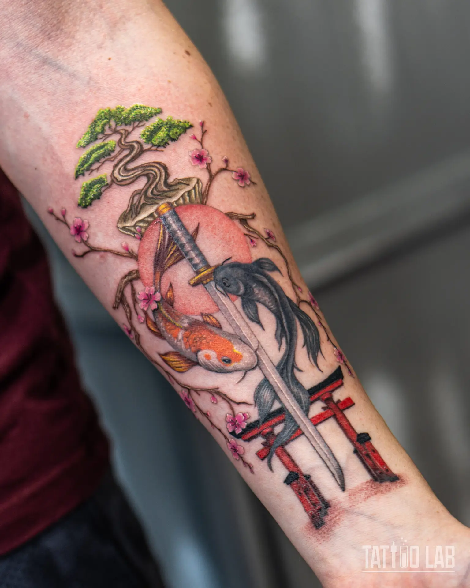 Colorful Japanese tattoo on forearm featuring koi fish, samurai sword, bonsai tree, cherry blossoms, and Torii gate — symbolizing balance, strength, and harmony, created at Tattoo Lab Halifax.