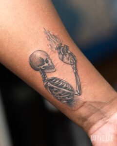 Black and grey skeleton tattoo on the forearm holding up an anatomical heart with rising smoke