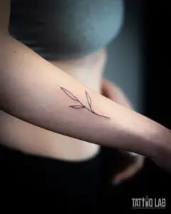 Minimalist fine line leaf sprig tattoo on the inner forearm in black ink