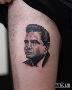 Black and grey realism portrait tattoo of Johnny Cash on the thigh with soft, detailed shading