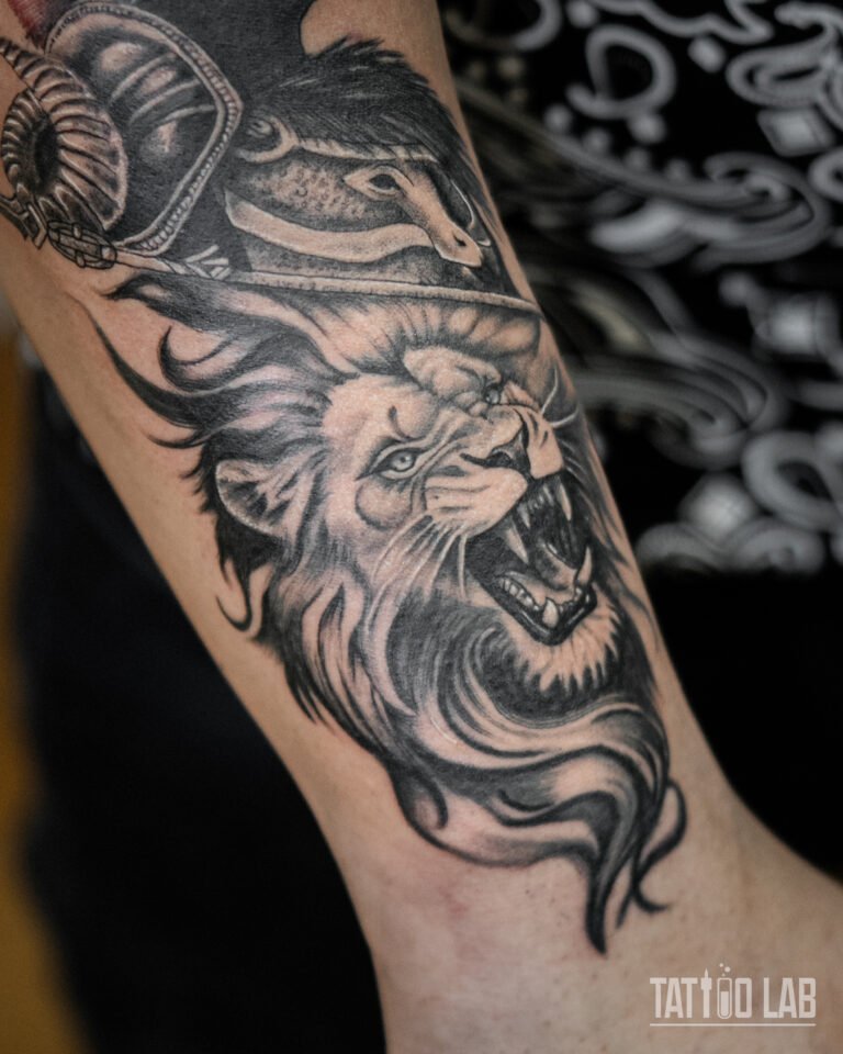 Black and grey roaring lion tattoo beneath a Spartan helmet, close-up of a realism arm piece