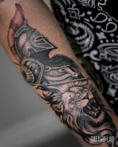 Realism Spartan helmet and roaring lion tattoo on the arm, black and grey with a red plume