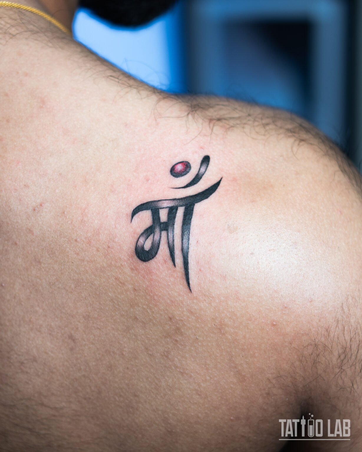 Hindi script Maa tattoo on the shoulder blade in black ink with a red dot accent, Tattoo Lab, Halifax