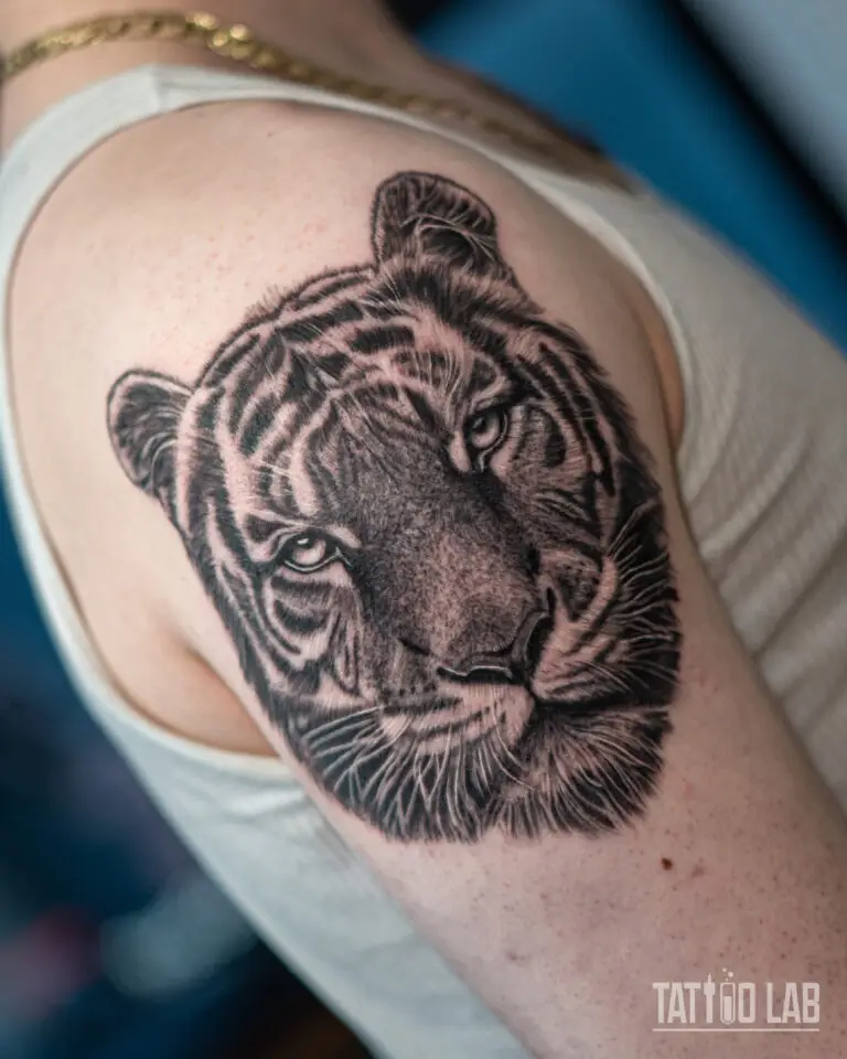 Black and grey realistic tiger head tattoo on the shoulder, angled view showing fur and whisker detail