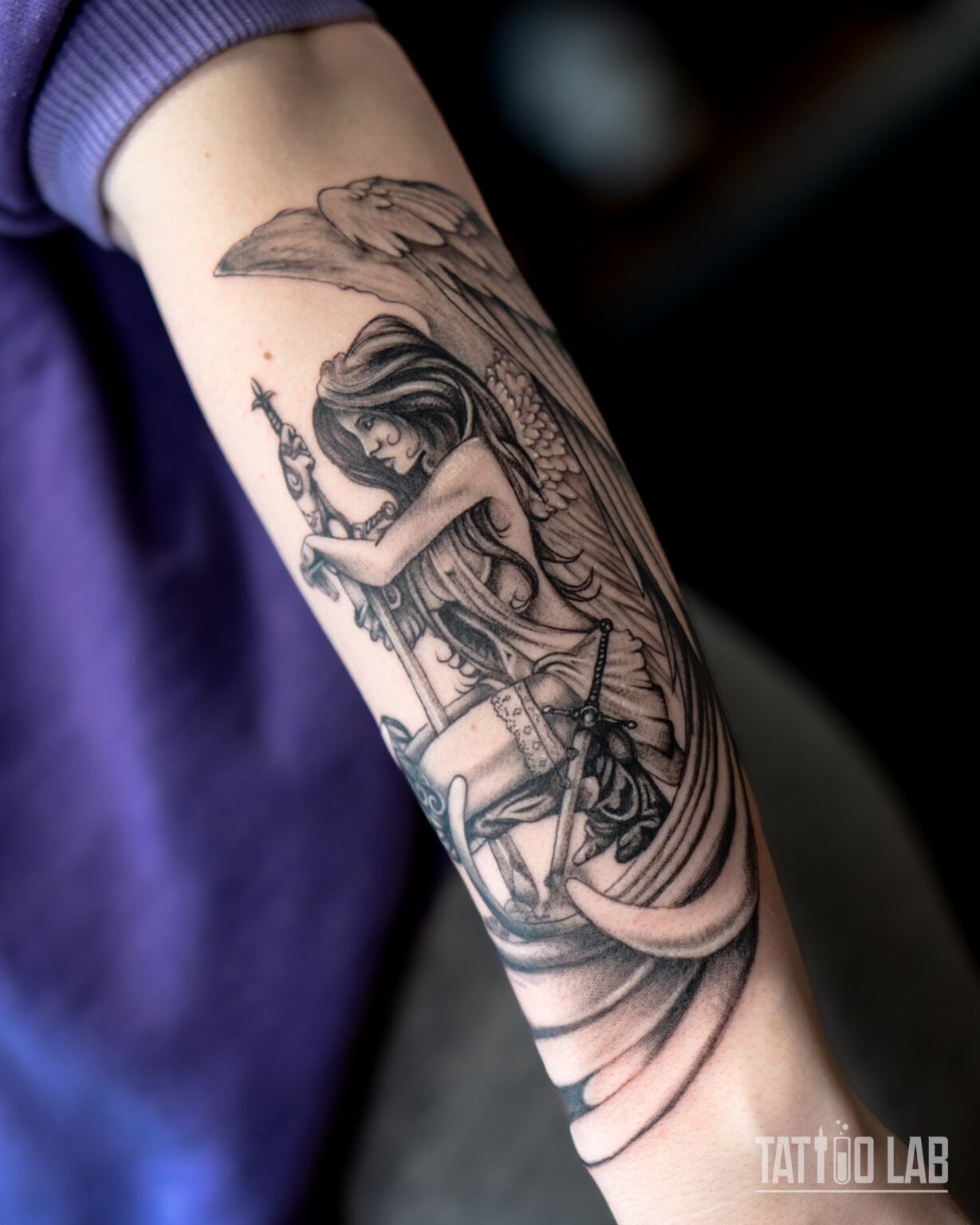 Black and grey angel tattoo on the forearm, a winged figure holding a sword wrapped in chains, Tattoo Lab, Halifax