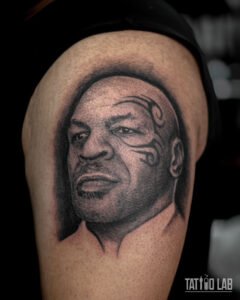 Black and grey realism portrait tattoo of Mike Tyson on the upper arm with detailed shading