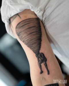 Surreal black and grey tattoo of a tornado swirling up from a hunched figure on the back of the arm