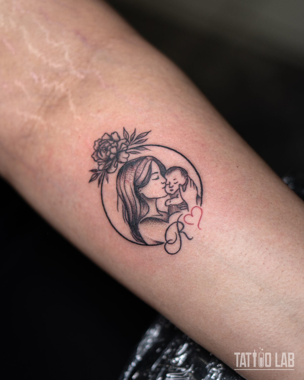 Fine line mother and baby tattoo in a circle frame with a peony, script initial and small red heart, Tattoo Lab, Halifax