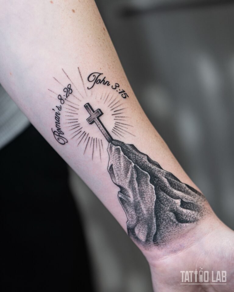 Angled view of a cross on a dotwork mountain peak tattoo with light rays on the inner forearm