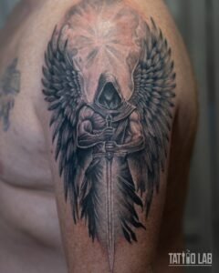Black and grey realism tattoo of a hooded winged angel holding a sword on the shoulder