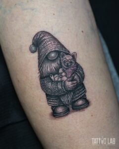 Gnome hugging a small dog tattoo in black and grey realism, with a light purple accent on the dog's sweater