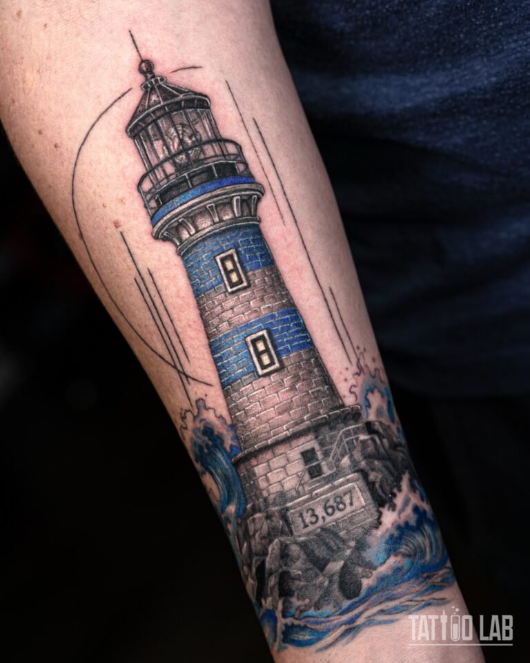 Angled close view of a black and grey lighthouse tattoo with blue bands and crashing blue waves on the forearm