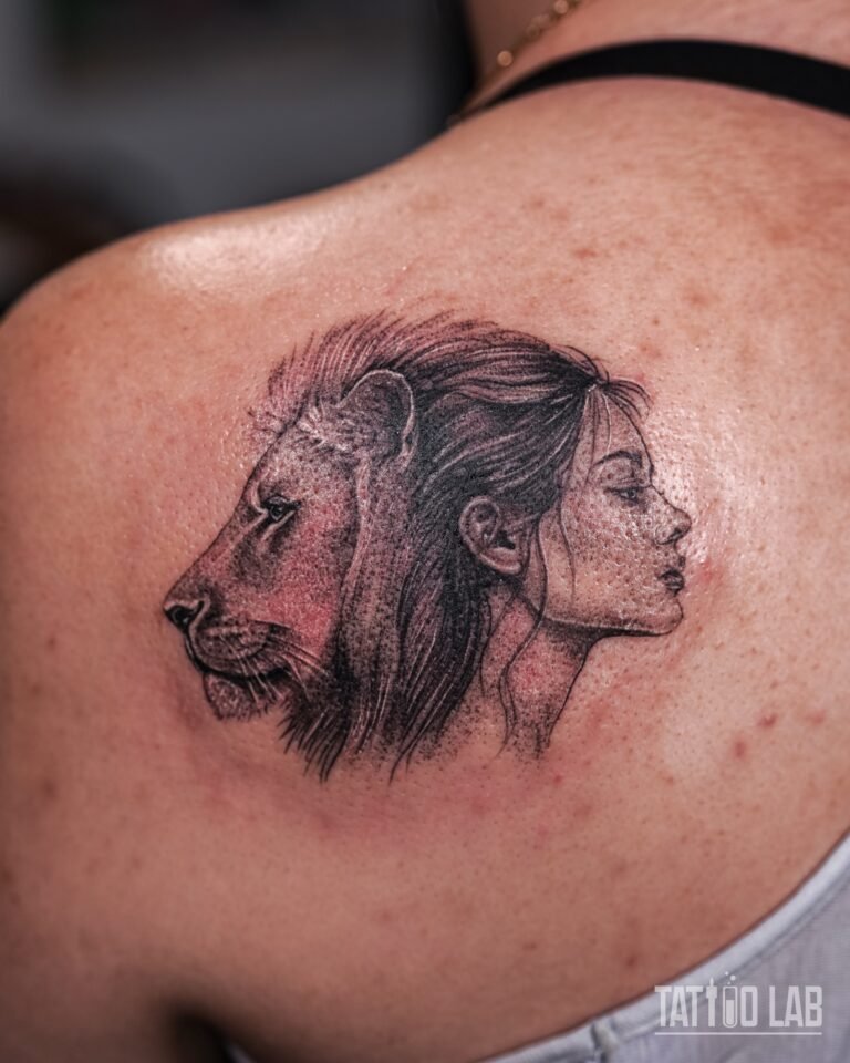 Wider view of a black and grey lion and woman profile tattoo on the shoulder blade
