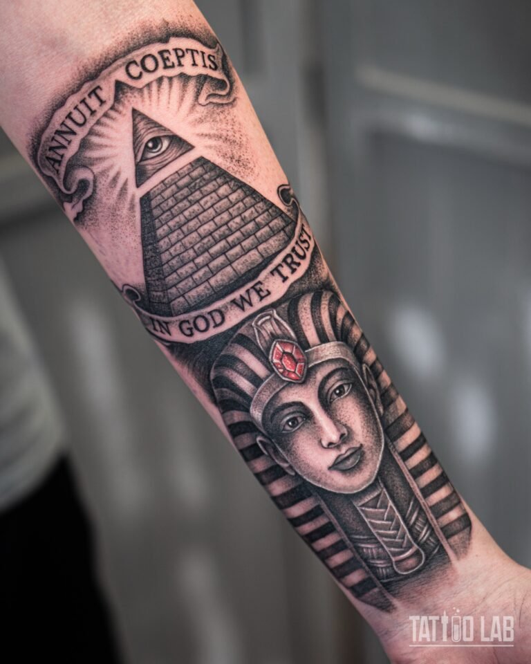 Angled view of a black and grey pharaoh tattoo below an all-seeing eye pyramid wrapping around the inner forearm