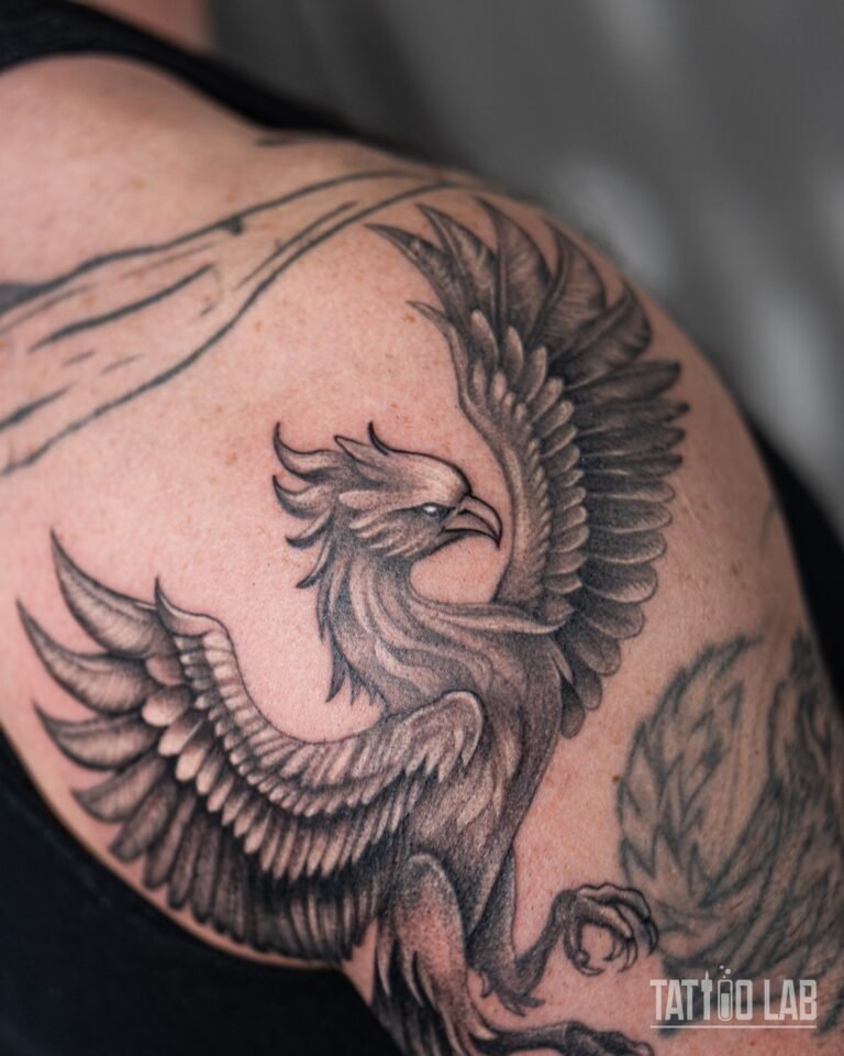 Close-up of a black and grey realism phoenix tattoo head and raised wings on the shoulder