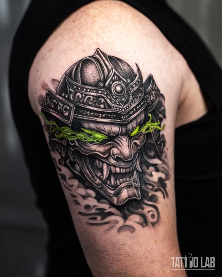 Black and grey realism tattoo of a samurai helmet and oni mask with glowing green eyes on the upper arm