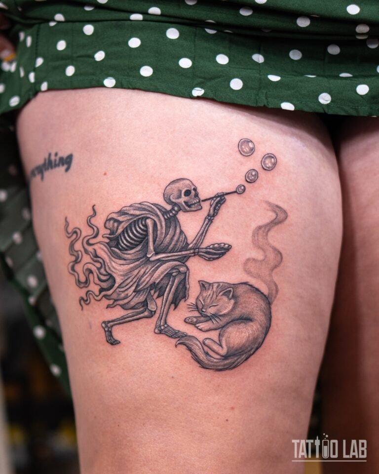 Black and grey tattoo of a robed skeleton blowing bubbles beside a sleeping cat, shown in full on the upper thigh