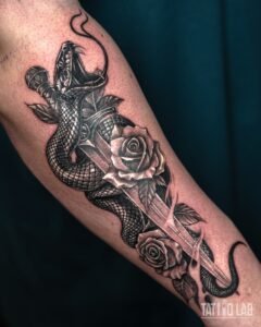 Black and grey realism tattoo of a snake coiled around a dagger with two roses and leaves on the forearm