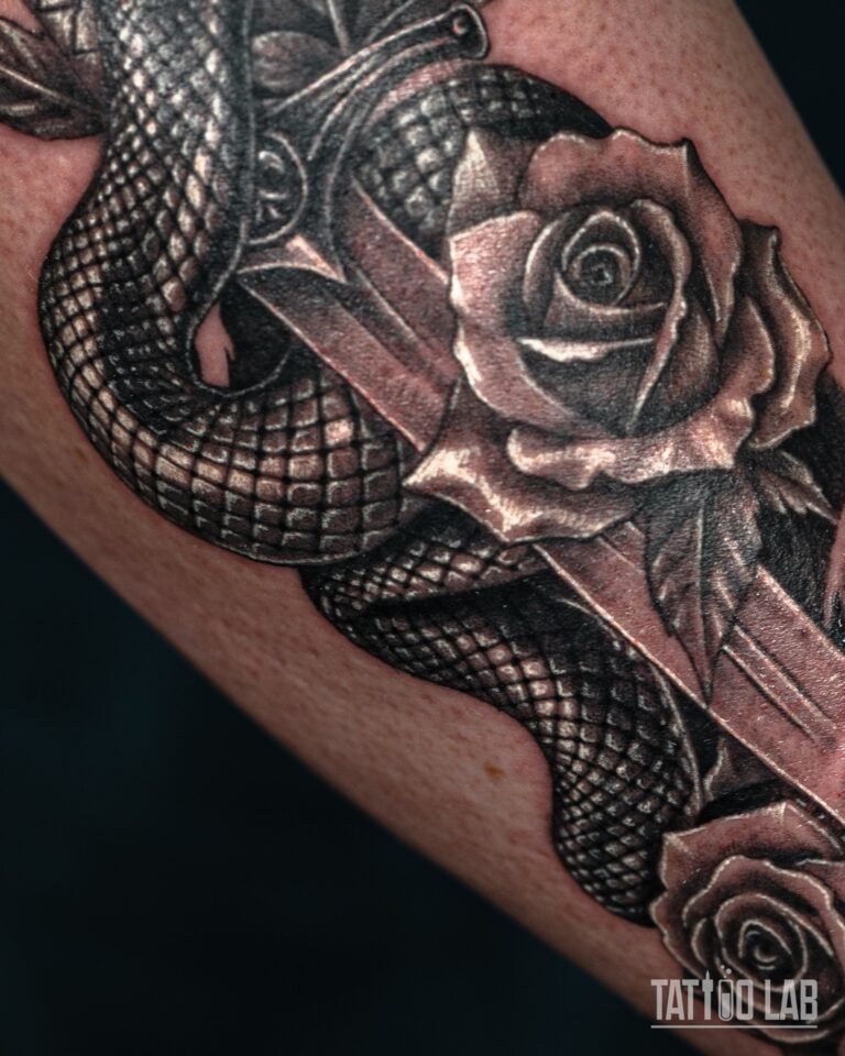 Close-up of black and grey rose petals and snake scale shading in a snake and dagger forearm tattoo
