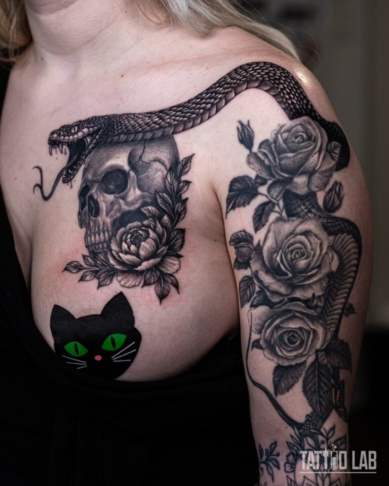 Black and grey realism chest piece of a snake and skull with peonies, continuing into a rose half sleeve on the upper arm