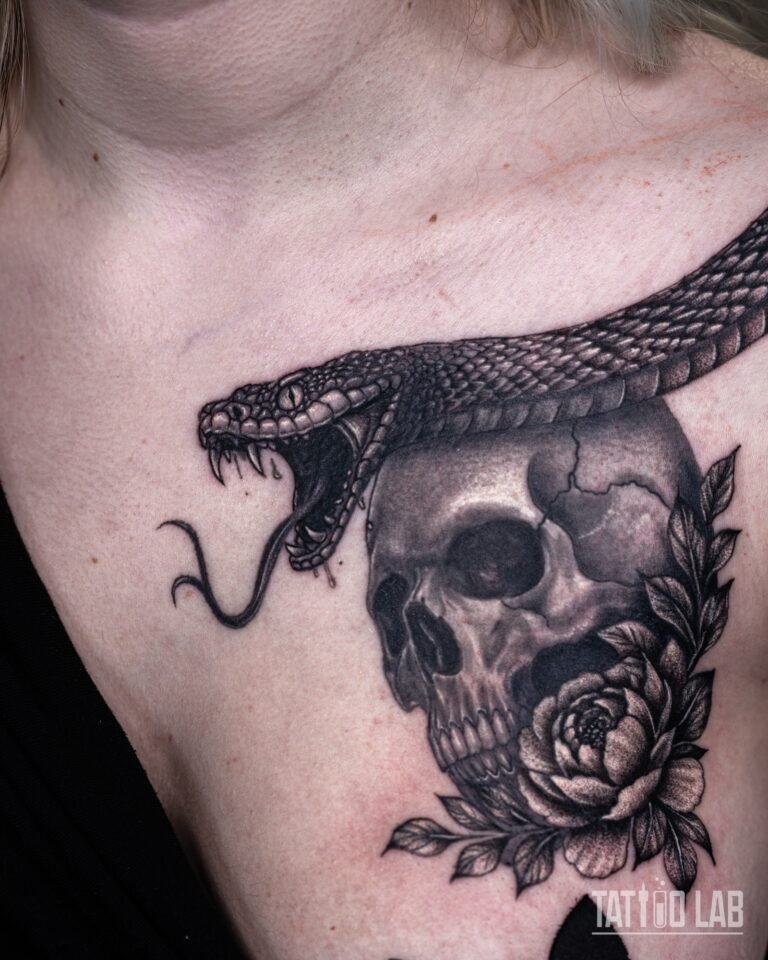 Black and grey realism tattoo of a striking snake over a cracked skull with a peony and leaves on the chest