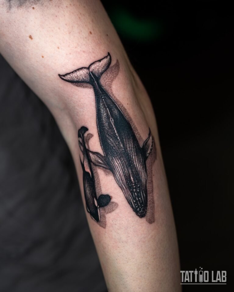 Angled view of a blackwork humpback whale and orca tattoo following the length of the forearm