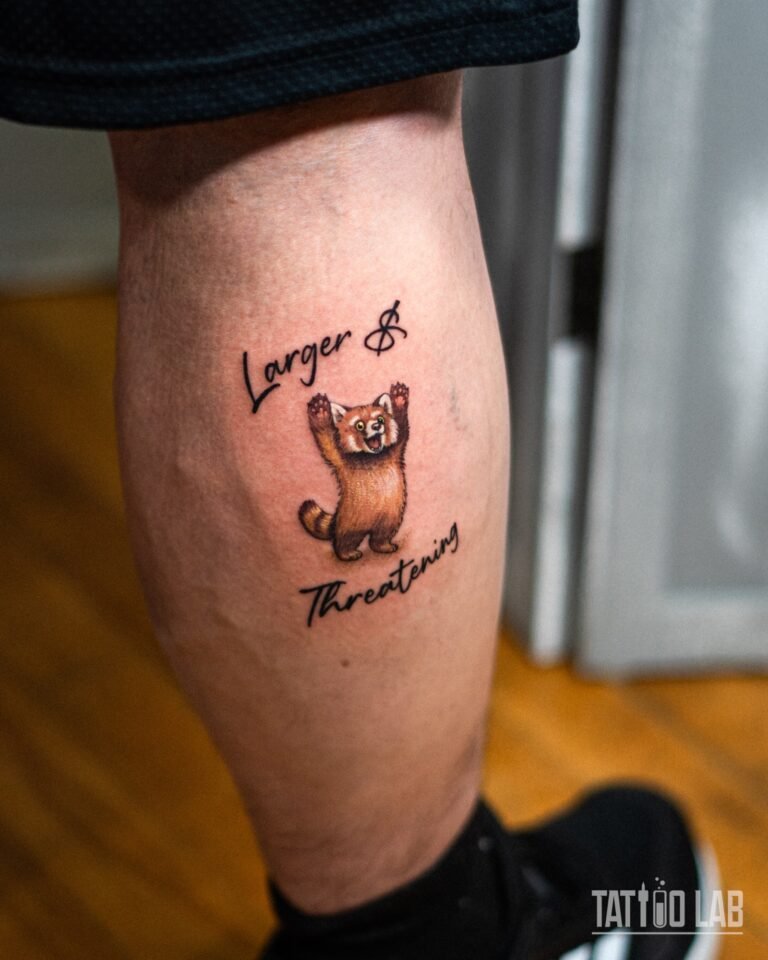 Wide view of a colour cartoon red panda tattoo with script lettering on the back of the calf