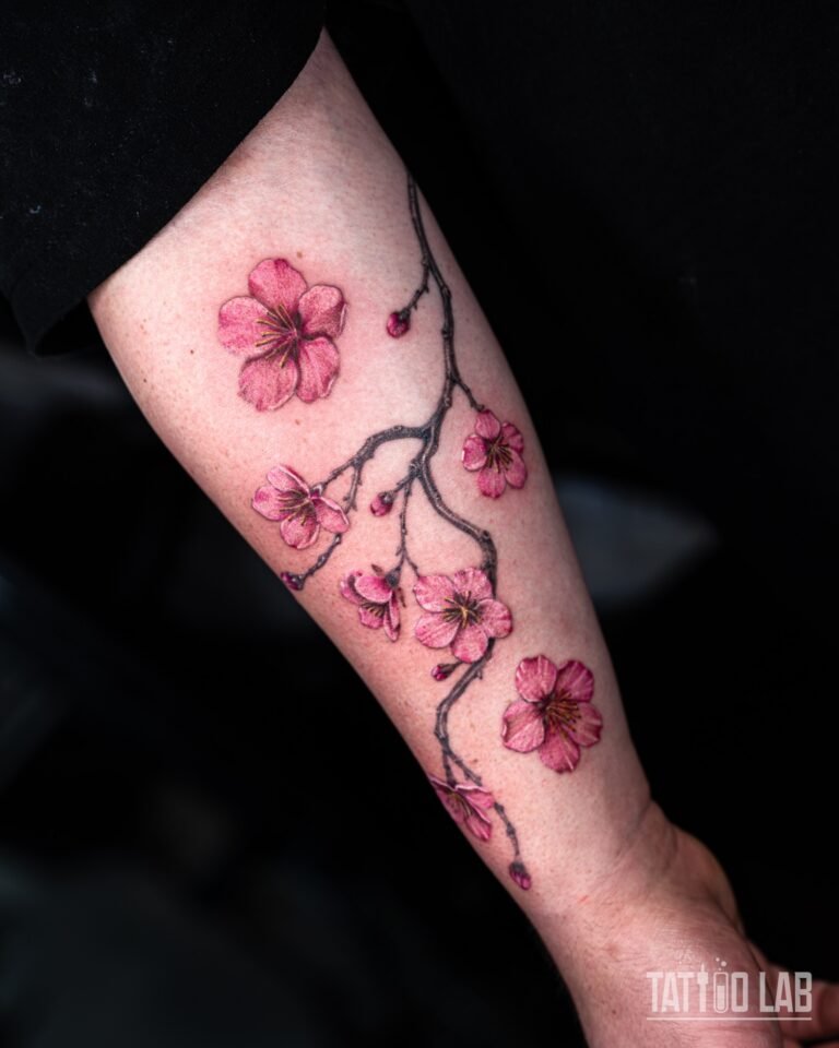 Pink cherry blossom branch tattoo in soft colour with grey shaded branches and buds along the inner forearm