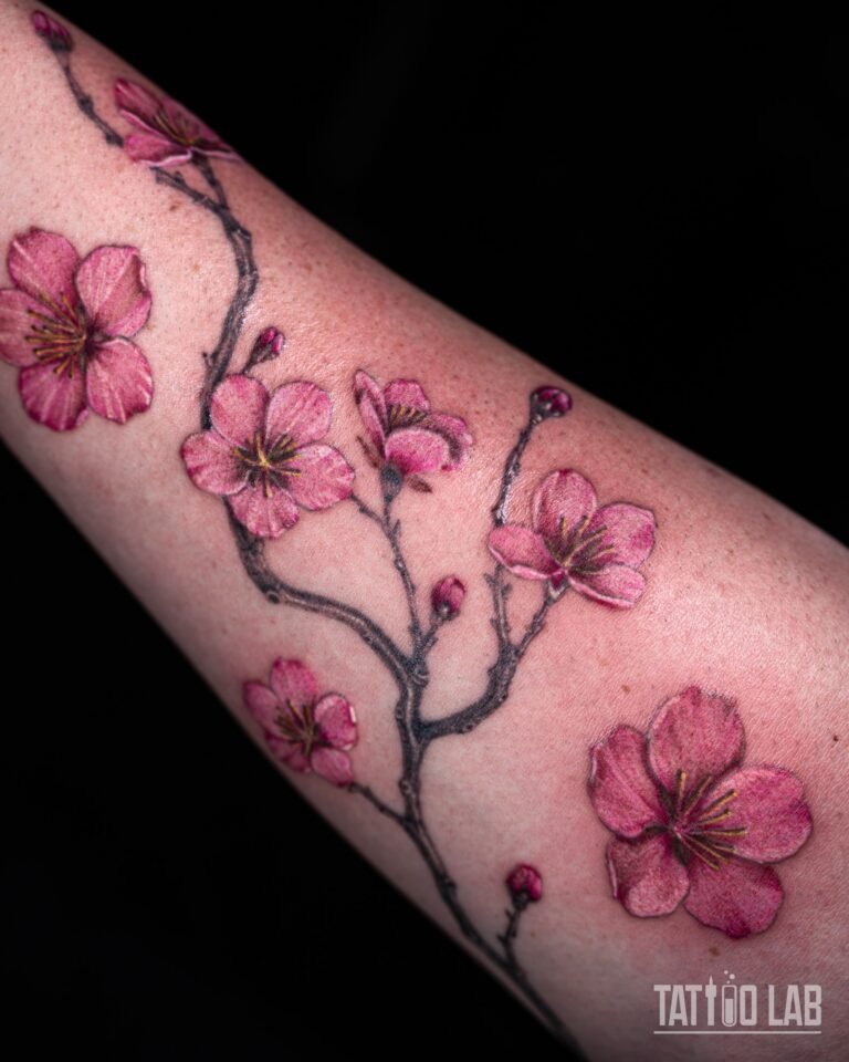 Close-up of pink cherry blossom tattoo flowers with yellow stamens and buds on a grey shaded branch