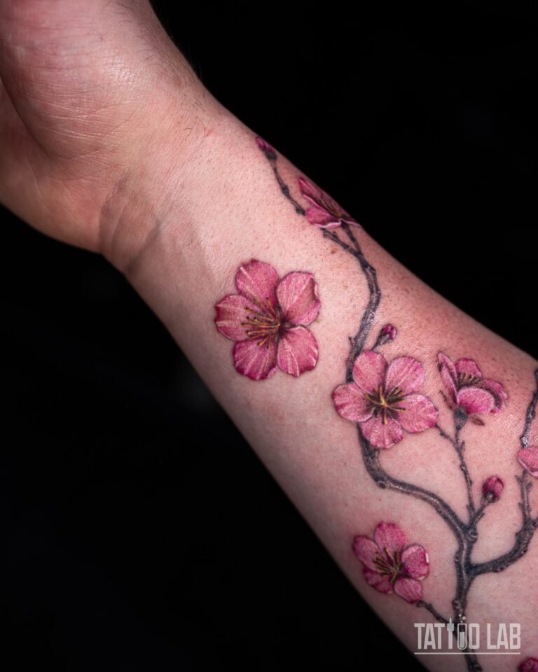 Close-up of pink cherry blossom tattoo flowers on a shaded branch near the wrist