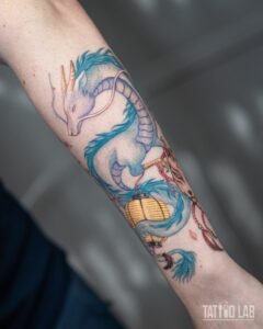 Pastel blue colour dragon tattoo holding a yellow paper lantern, anime-inspired forearm sleeve