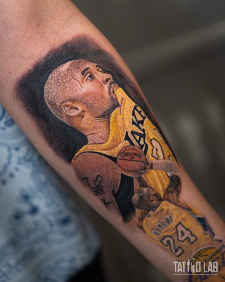 Close-up of a colour realism Kobe Bryant portrait tattoo with detailed skin tones, a gold Lakers jersey and a basketball